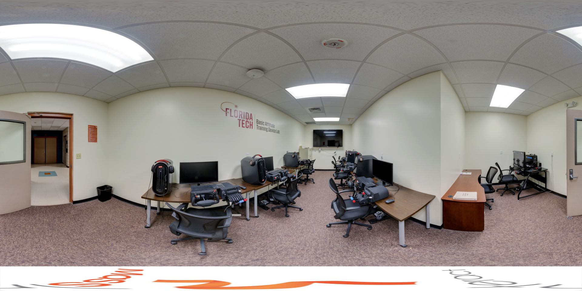 Panoramic view of a flight training lab with multiple flight simulator stations set up for students, under a curved ceiling with ambient lighting